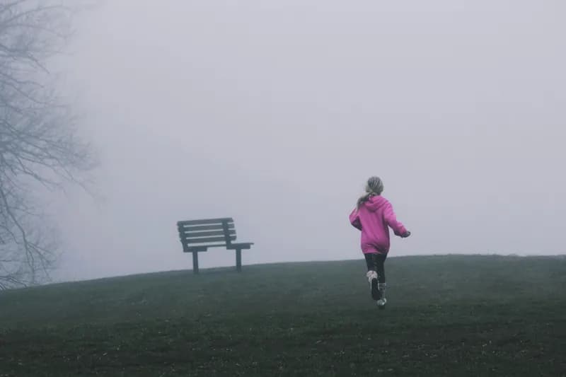A girl running on a hill surrounded by thick fog.