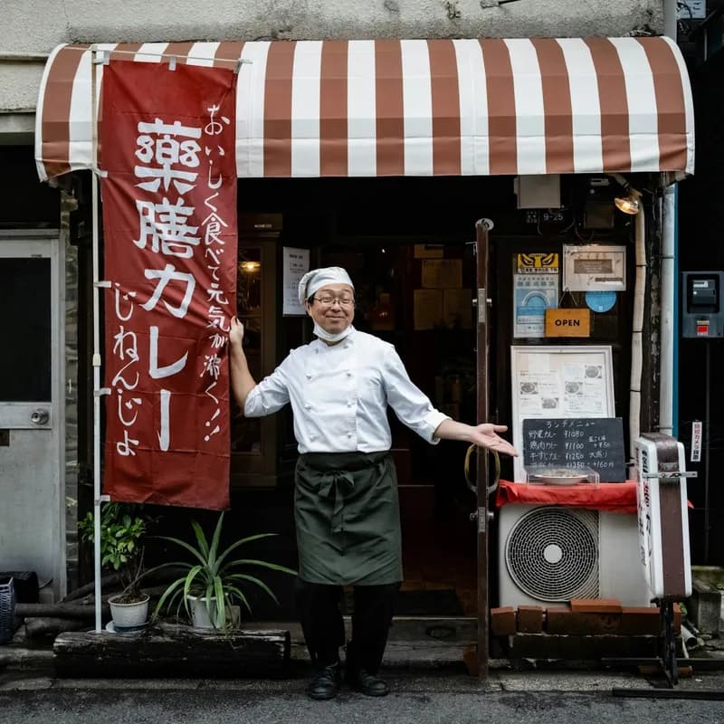 A Japaneseman smiles in front of a curry restaurant with a sign that says open.