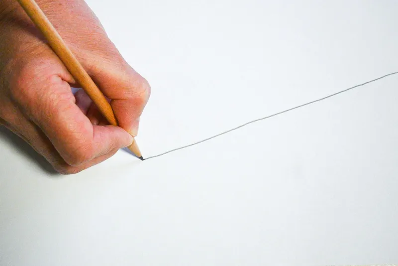 Hand holding a pencil drawing a thin straight line on white paper