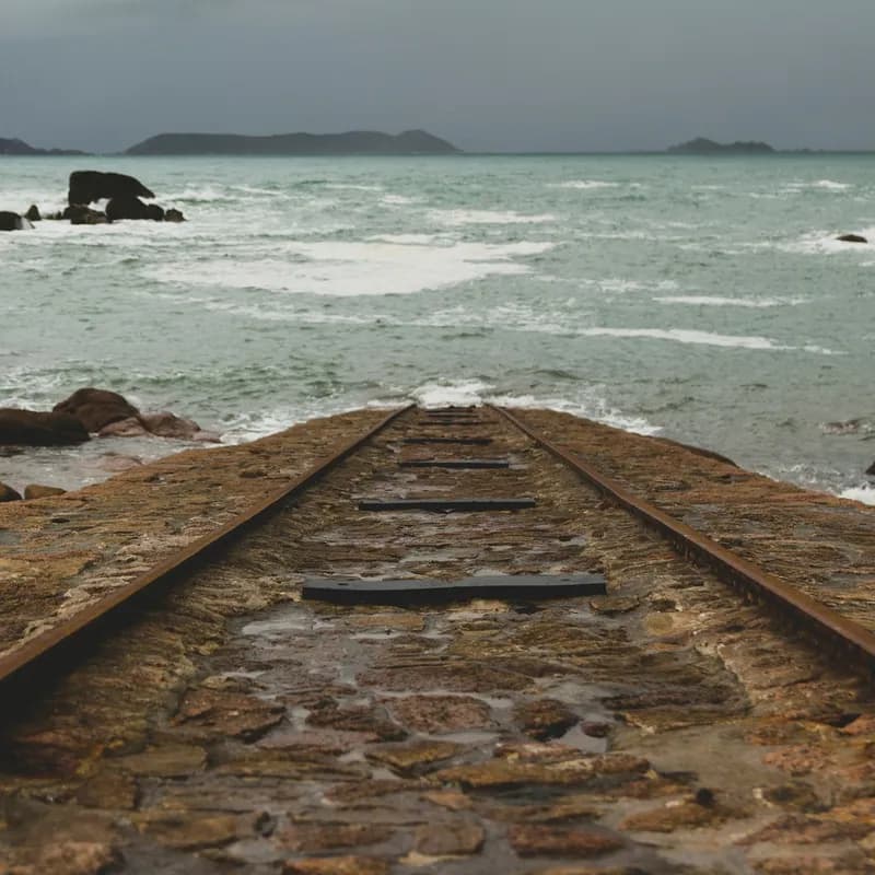 Photograph of an old stone path ending abruptly into the waves of the sea.