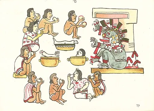 Historical illustration of Aztec human sacrifice ritual, in which several people are sitting in a circle eating white spherical objects, several severed body parts are displayed on large bowls, and a mythical monster-like creature shakes its hands towards them.
