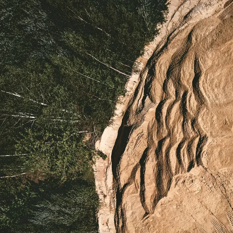 Picture taken from above of a forest, with trees on one side and what seems like an excavation site, dunes of dirt without any vegetation, on the other side, separated by a sharp boundary.