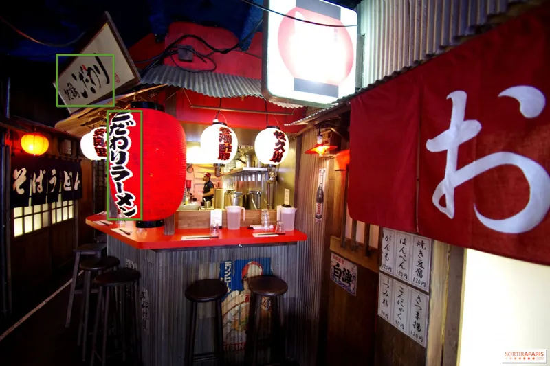 A picture of a ramen stand, with the word kodawari highlighted in the restaurant's banner and on a lantern. A ramen stand titled "Native Fowl Kodawari". The lantern says "Kodawari ramen".